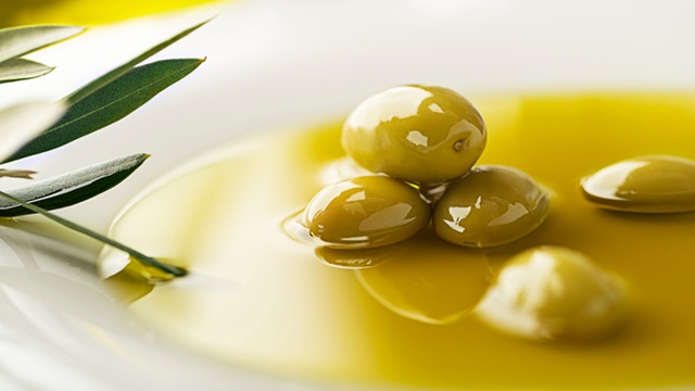Green and black olives submerged in golden olive oil inside a glass bowl